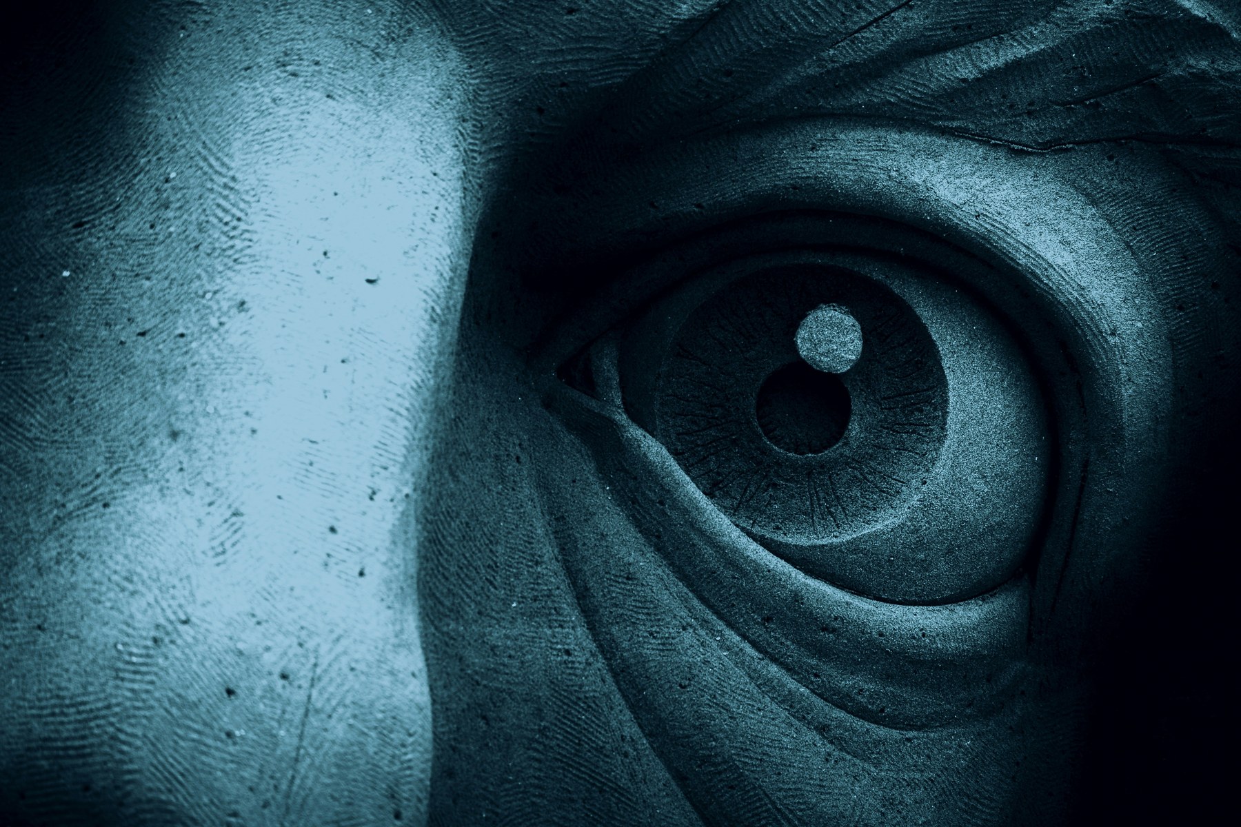 Blue-toned close-up of a carved stone eye on a classical sculpture.
